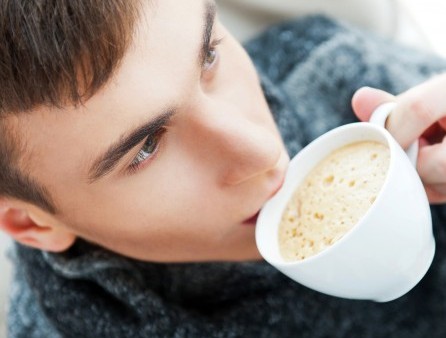 Portrait of a young man drinking coffee while sitting on armchai